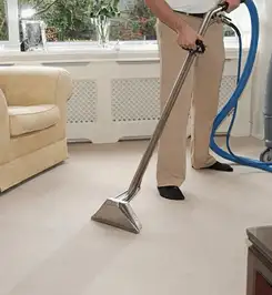 Professional carpet cleaner using a hot-water extraction wand and hose machine in a living room in Houston, TX.